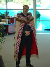 Saul standing wearing his whānau korowai and pounamu in the shape of a tooth/niho.