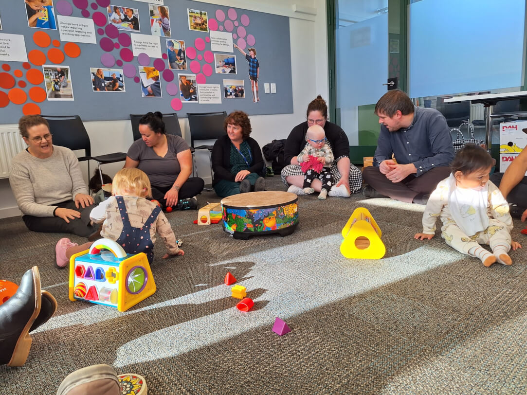 Figure 1 - Adults and children are sitting on the floor surrounded by toys