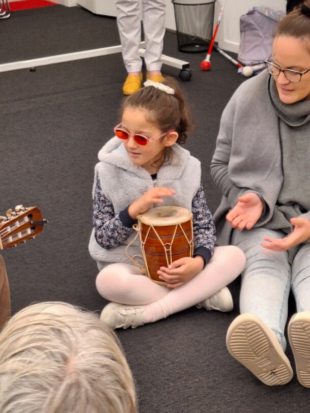 Figure 2 - Dima is sitting on the floor playing a hand drum alongside a first year Music therapist.