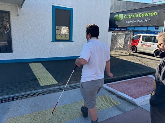 Figure 1 - Learner is holding a cane and walking across yellow dots on the footpath and street