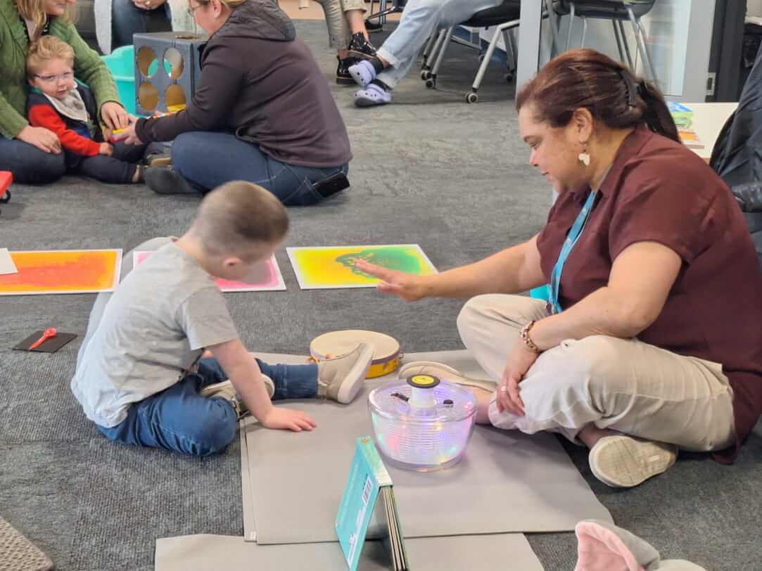 Figure 1 - Boy on floor looking at tambourine with adult tapping a tambourine 