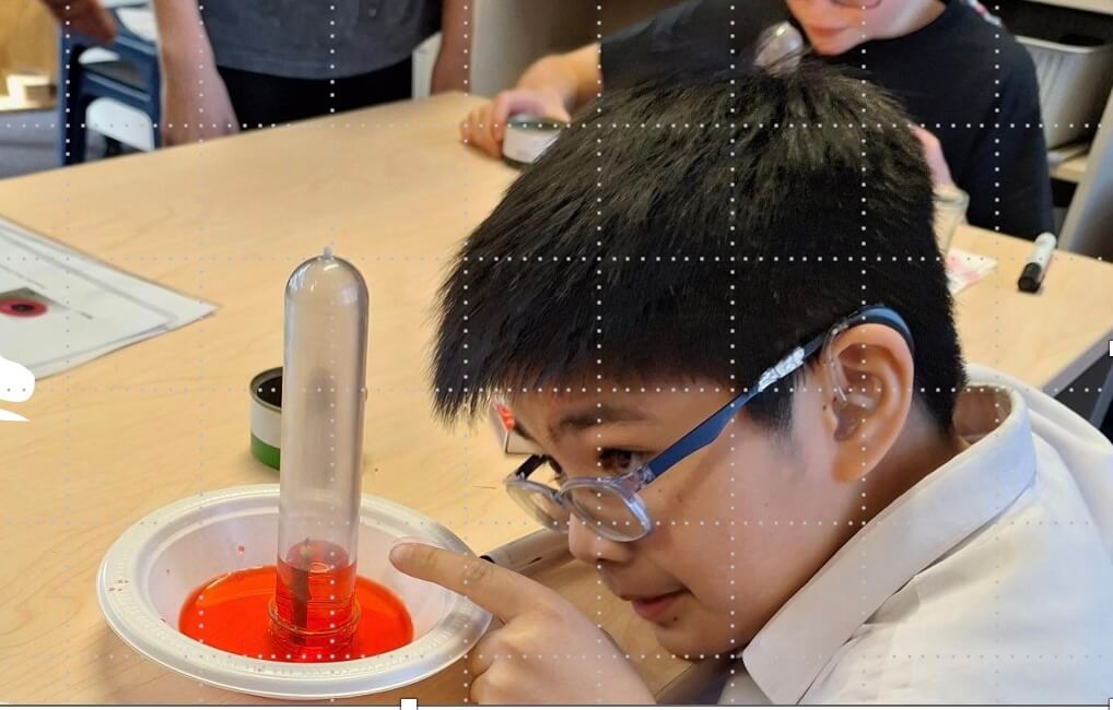 Figure 2 - Ākonga sitting at table with a white bowl containing red liquid and a test tube