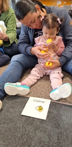 Figure 2 - Little girl sitting on mat with mum behind her, feeling plastic yellow ducks